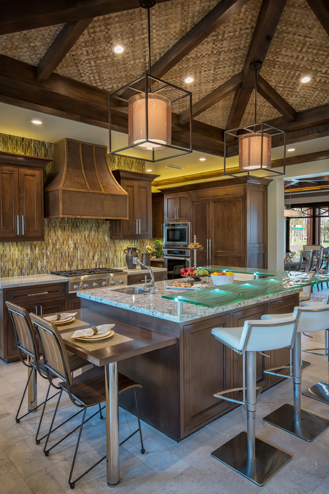 Design ideas for a mid-sized tropical u-shaped open plan kitchen in San Diego with a double-bowl sink, recessed-panel cabinets, dark wood cabinets, granite benchtops, green splashback, glass tile splashback, stainless steel appliances, travertine floors and with island.