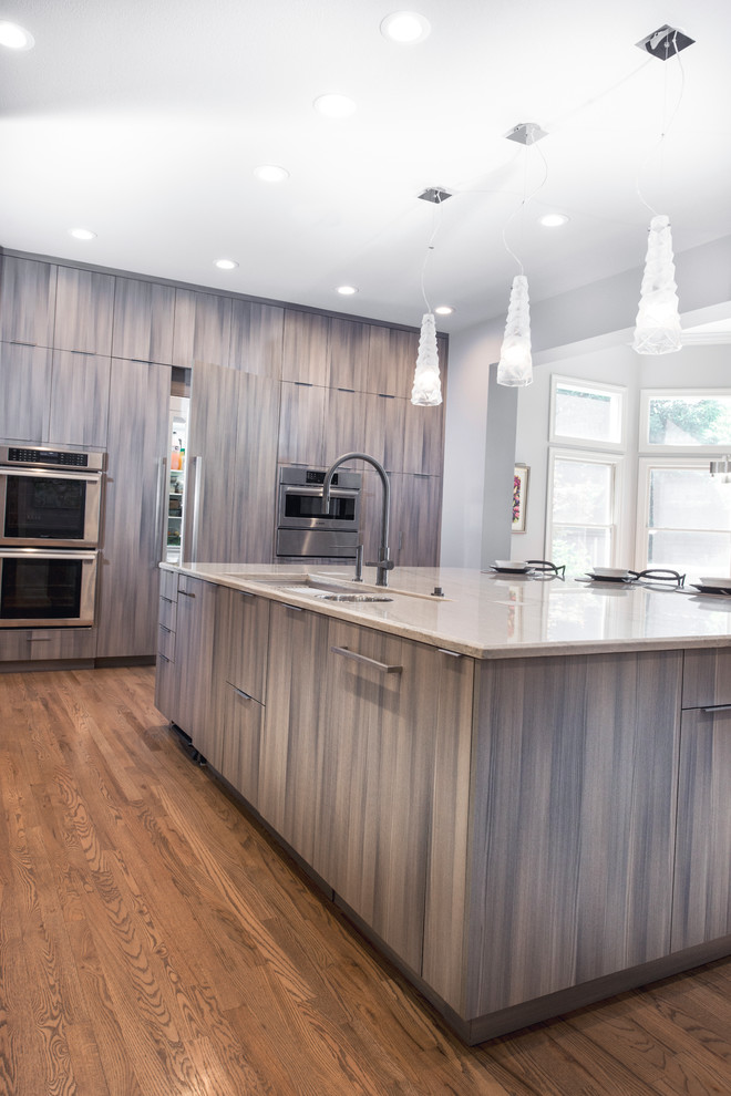 Example of a large transitional medium tone wood floor and brown floor open concept kitchen design with an undermount sink, flat-panel cabinets, brown cabinets, quartzite countertops, white backsplash, ceramic backsplash, stainless steel appliances, an island and beige countertops