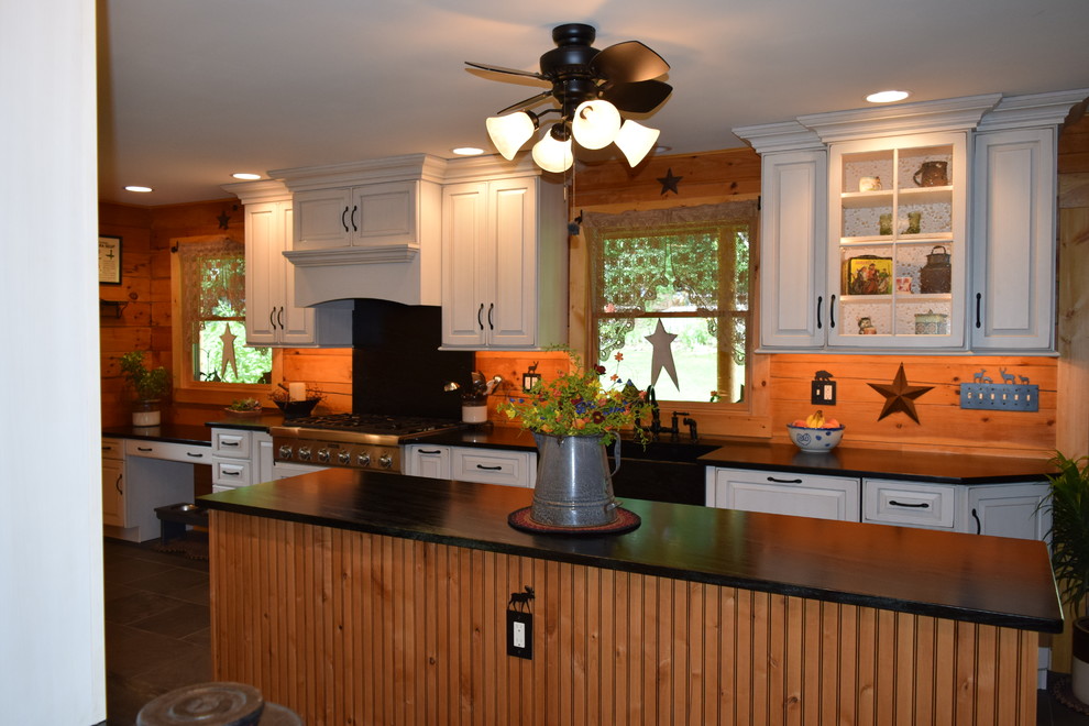 Large mountain style galley slate floor eat-in kitchen photo with a farmhouse sink, raised-panel cabinets, white cabinets, soapstone countertops, stainless steel appliances and an island