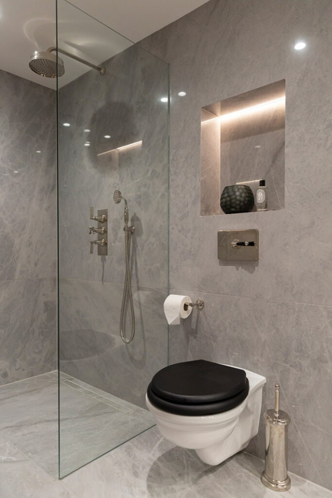 This is an example of a large modern 3/4 bathroom in London with grey cabinets, a drop-in tub, a shower/bathtub combo, an urinal, gray tile, glass tile, grey walls, ceramic floors, a drop-in sink, stainless steel benchtops, grey floor, a hinged shower door, brown benchtops, a single vanity, a floating vanity, wood, decorative wall panelling and open cabinets.