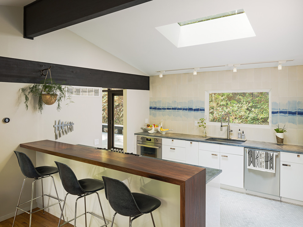 Midcentury single-wall open plan kitchen in Philadelphia with an undermount sink, flat-panel cabinets, white cabinets, wood benchtops, beige splashback, ceramic splashback, stainless steel appliances, marble floors, with island and white floor.