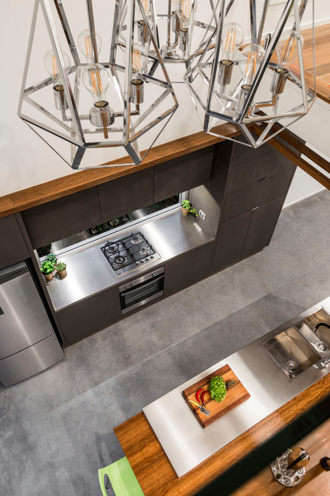 Small modern galley open plan kitchen in Brisbane with flat-panel cabinets, grey cabinets, stainless steel benchtops, glass sheet splashback, stainless steel appliances, concrete floors, with island and grey floor.