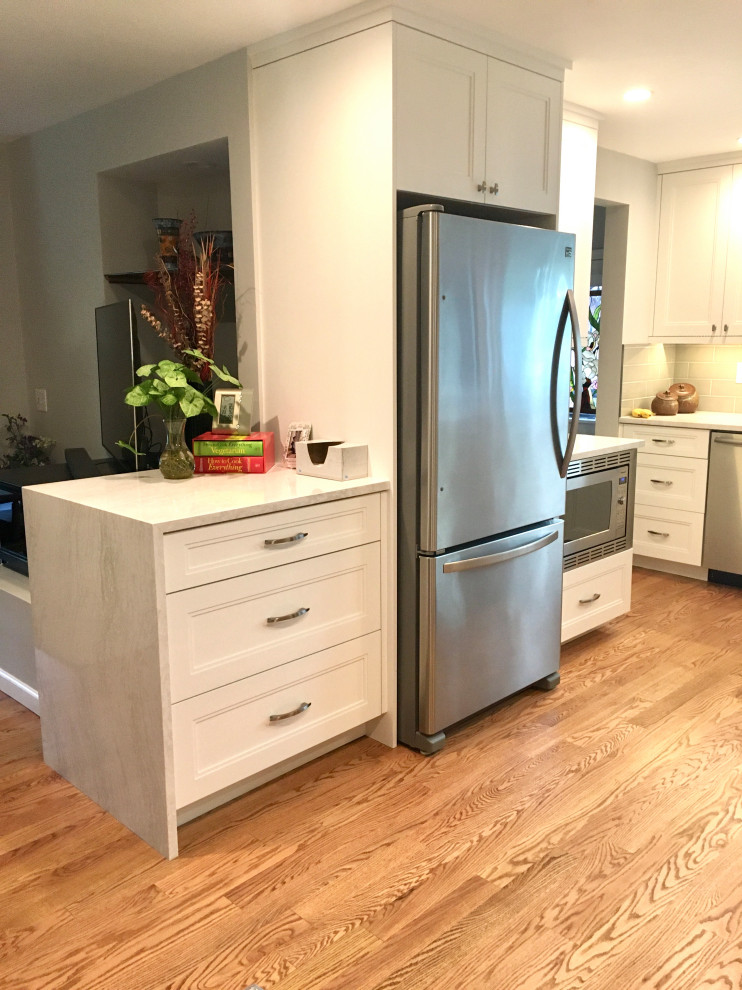 Example of a small transitional u-shaped medium tone wood floor and brown floor enclosed kitchen design in Denver with a drop-in sink, shaker cabinets, white cabinets, quartz countertops, gray backsplash, subway tile backsplash, stainless steel appliances, a peninsula and white countertops