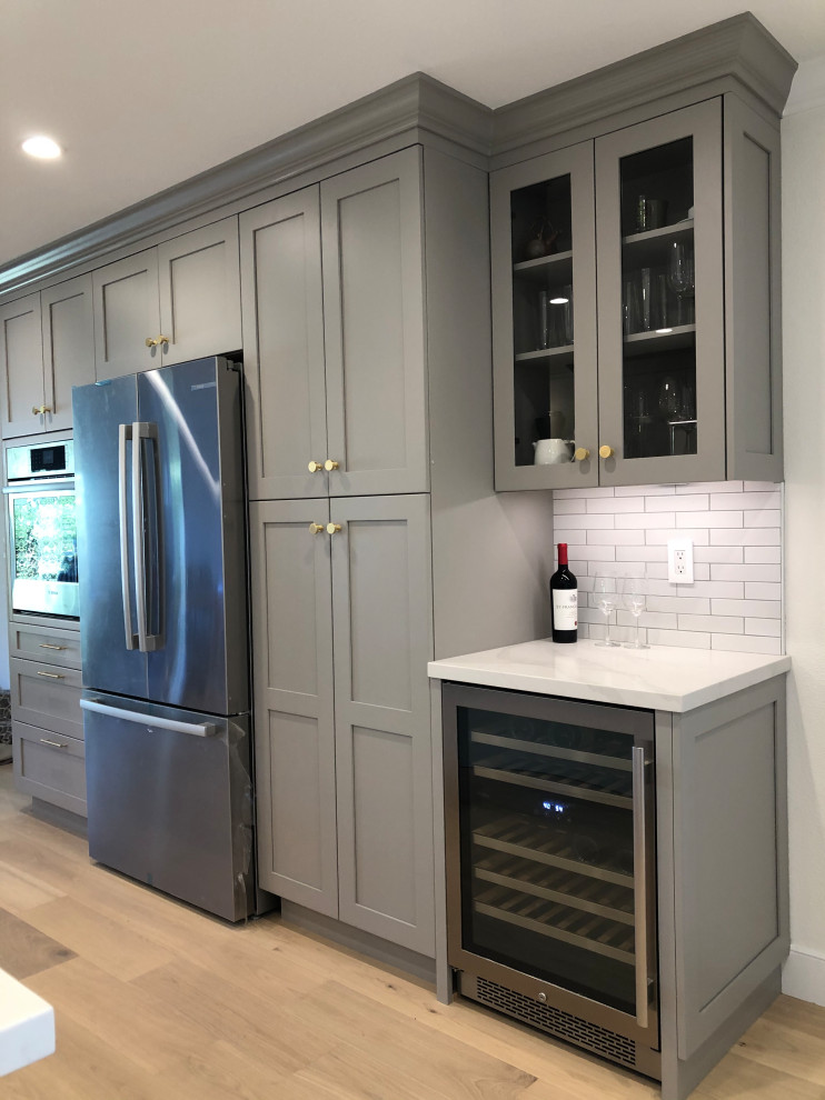 Eat-in kitchen - mid-sized transitional galley medium tone wood floor and beige floor eat-in kitchen idea in San Francisco with an undermount sink, recessed-panel cabinets, gray cabinets, quartz countertops, white backsplash, ceramic backsplash, stainless steel appliances, an island and white countertops