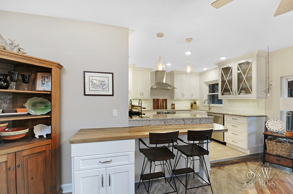 Example of a mid-sized transitional galley porcelain tile and gray floor eat-in kitchen design in Tampa with a farmhouse sink, flat-panel cabinets, white cabinets, wood countertops, white backsplash, subway tile backsplash, stainless steel appliances, a peninsula and beige countertops