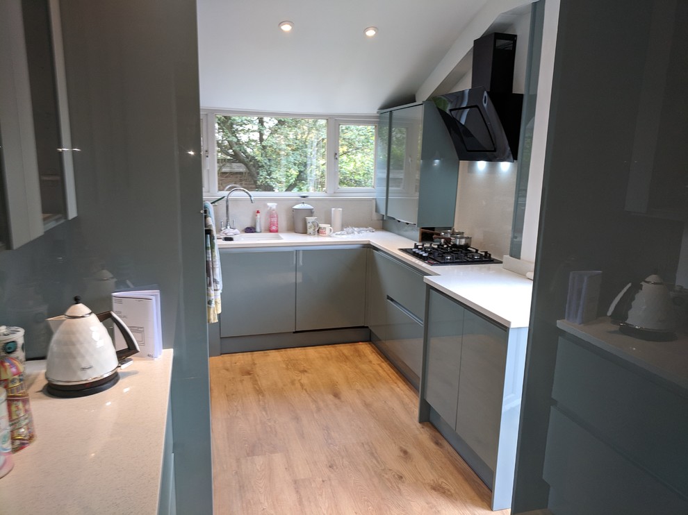 Photo of a mid-sized modern u-shaped separate kitchen in London with an undermount sink, flat-panel cabinets, turquoise cabinets, quartzite benchtops, white splashback, stone slab splashback, black appliances, vinyl floors, no island, brown floor and white benchtop.