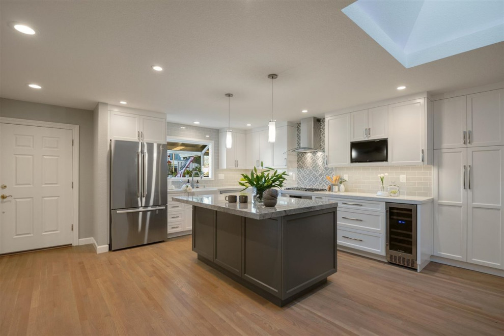 This is an example of a medium sized modern grey and white l-shaped open plan kitchen in San Francisco with a belfast sink, shaker cabinets, white cabinets, engineered stone countertops, grey splashback, ceramic splashback, stainless steel appliances, medium hardwood flooring, an island, grey floors and grey worktops.