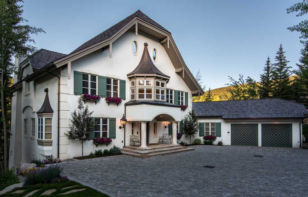 This is an example of a large traditional two-storey stucco white house exterior in Denver with a shingle roof, a clipped gable roof and a black roof.