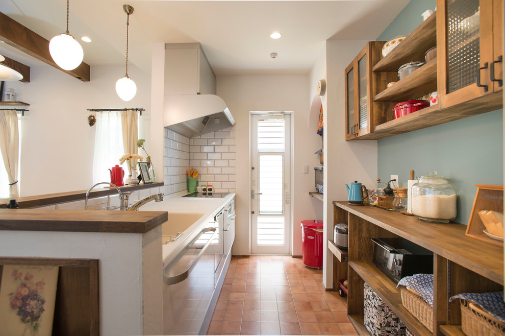 Asian galley open plan kitchen in Nagoya with an integrated sink, open cabinets, white splashback, terra-cotta floors, with island and brown floor.