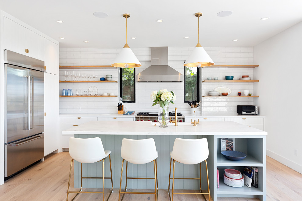Inspiration for a large contemporary single-wall open plan kitchen in Los Angeles with a farmhouse sink, flat-panel cabinets, blue cabinets, quartz benchtops, white splashback, porcelain splashback, stainless steel appliances, light hardwood floors, with island, beige floor and white benchtop.