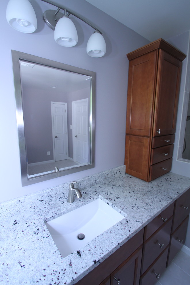 Large transitional master bathroom in DC Metro with an undermount sink, dark wood cabinets, granite benchtops, white tile, porcelain tile, purple walls, a corner shower and porcelain floors.