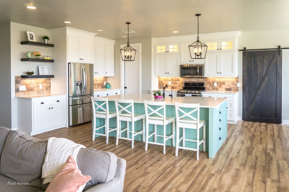 Inspiration for a mid-sized l-shaped medium tone wood floor and brown floor open concept kitchen remodel with a drop-in sink, shaker cabinets, white cabinets, brown backsplash, stone tile backsplash, stainless steel appliances and an island