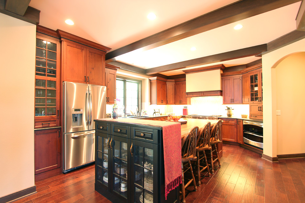 This is an example of a large traditional l-shaped open plan kitchen in Other with an undermount sink, recessed-panel cabinets, medium wood cabinets, granite benchtops, white splashback, porcelain splashback, stainless steel appliances, medium hardwood floors, with island, brown floor and black benchtop.