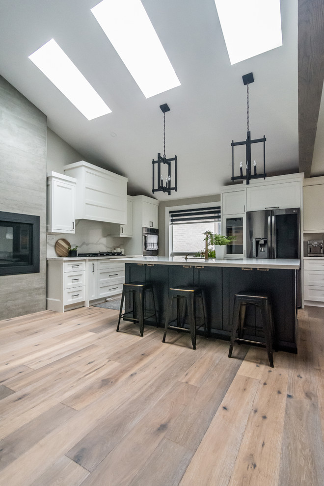 Design ideas for a large transitional l-shaped eat-in kitchen in Toronto with an undermount sink, shaker cabinets, white cabinets, quartz benchtops, white splashback, stone slab splashback, black appliances, medium hardwood floors, with island, brown floor and white benchtop.