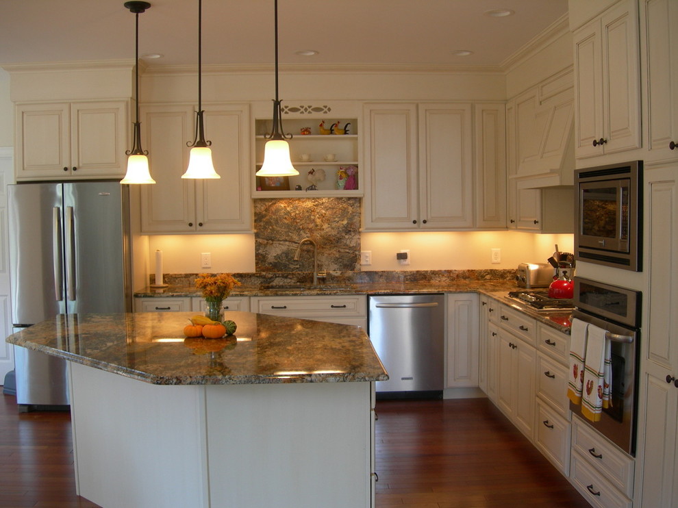 Inspiration for a large transitional l-shaped dark wood floor eat-in kitchen remodel in Burlington with an undermount sink, raised-panel cabinets, white cabinets, granite countertops, brown backsplash, stone slab backsplash, stainless steel appliances and an island