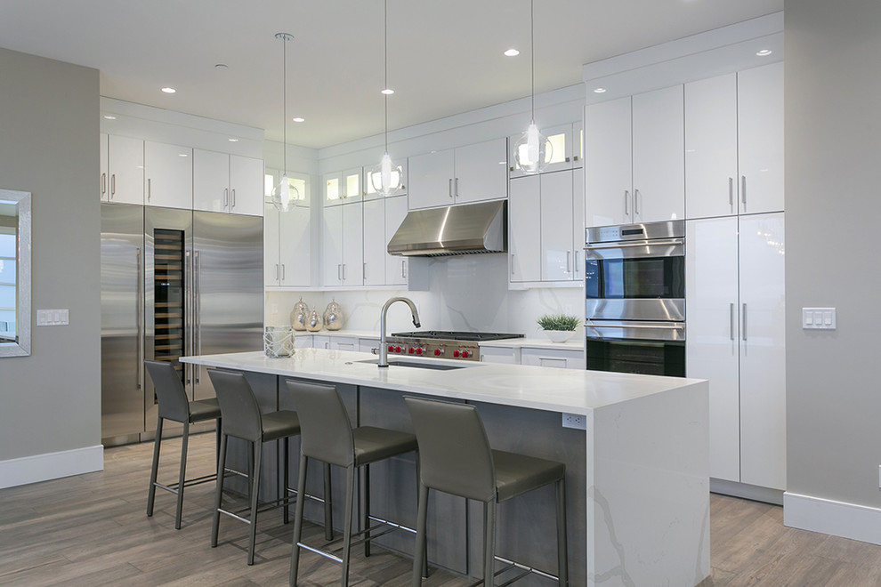 Large contemporary u-shaped eat-in kitchen in Vancouver with an undermount sink, flat-panel cabinets, white cabinets, quartz benchtops, white splashback, stone slab splashback, stainless steel appliances, light hardwood floors, with island, grey floor and white benchtop.