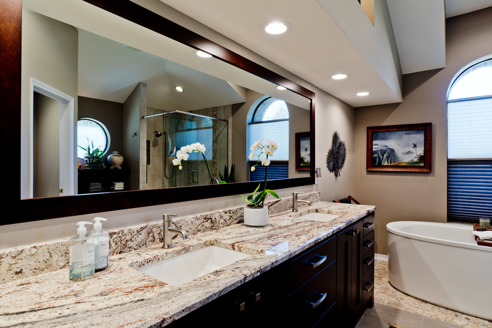 Photo of a large asian master bathroom in Miami with shaker cabinets, dark wood cabinets, a freestanding tub, a curbless shower, a two-piece toilet, gray tile, porcelain tile, beige walls, porcelain floors, an undermount sink and granite benchtops.