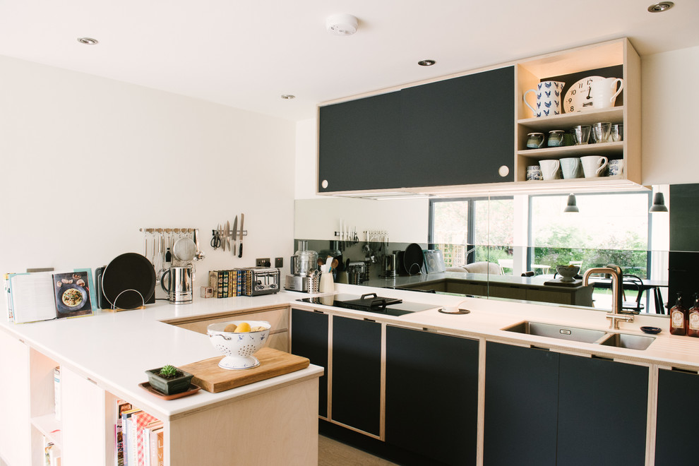 This is an example of a small contemporary u-shaped kitchen in Other with a double-bowl sink, flat-panel cabinets, mirror splashback, white benchtop, black cabinets, black appliances and a peninsula.