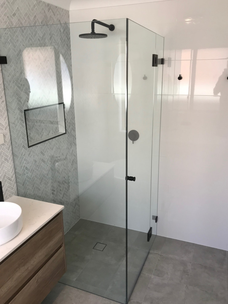 Photo of a mid-sized beach style master bathroom in Sydney with flat-panel cabinets, medium wood cabinets, a freestanding tub, a corner shower, gray tile, marble, white walls, porcelain floors, a vessel sink, engineered quartz benchtops, grey floor, a hinged shower door, white benchtops, a niche, a single vanity and a floating vanity.
