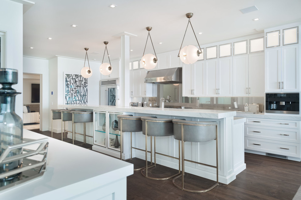 Large beach style u-shaped open plan kitchen in Los Angeles with an undermount sink, recessed-panel cabinets, white cabinets, marble benchtops, multi-coloured splashback, glass sheet splashback, stainless steel appliances, dark hardwood floors, with island, brown floor and white benchtop.