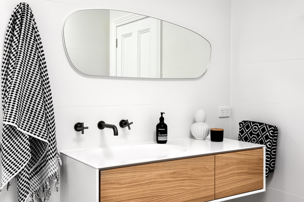 Inspiration for a mid-sized contemporary bathroom in Sydney with flat-panel cabinets, medium wood cabinets, white tile, white walls, an integrated sink, white benchtops, porcelain tile, porcelain floors, solid surface benchtops and grey floor.