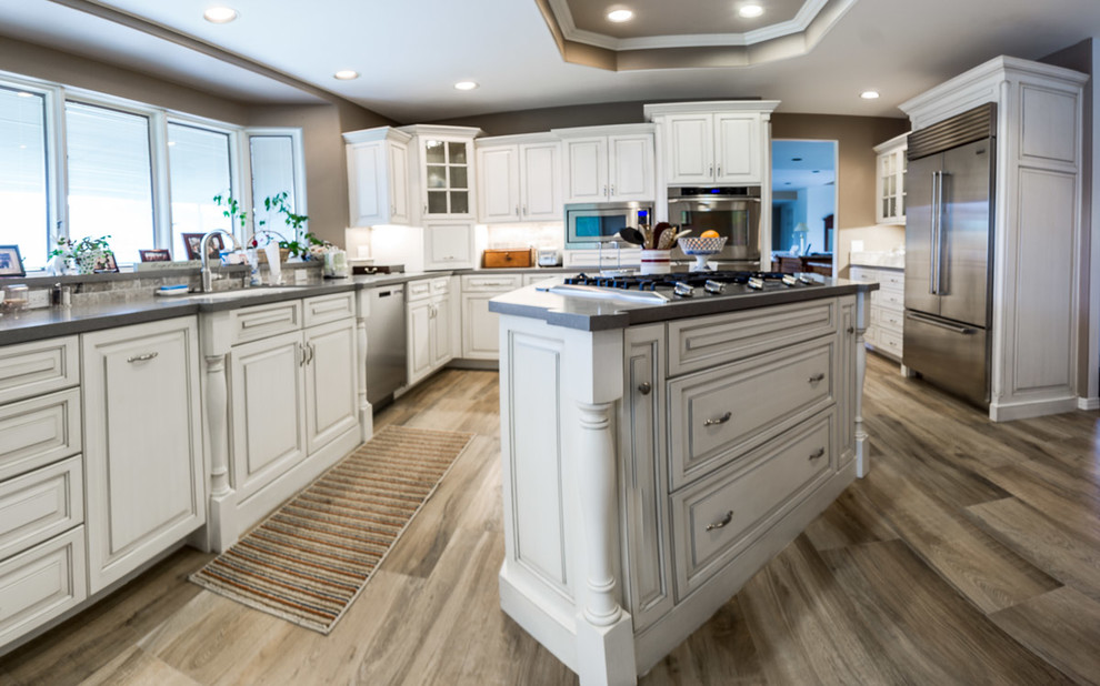 Photo of a large transitional u-shaped eat-in kitchen in San Diego with a single-bowl sink, raised-panel cabinets, white cabinets, quartzite benchtops, beige splashback, travertine splashback, stainless steel appliances, porcelain floors, with island and multi-coloured floor.