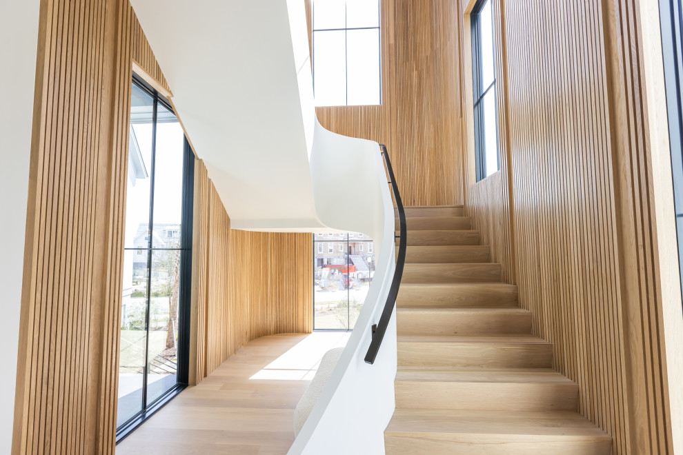 Cette image montre un grand escalier courbe minimaliste en bois avec des marches en bois, des contremarches en bois et un garde-corps en matériaux mixtes.