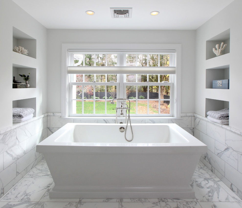 Photo of a large traditional master bathroom in Other with recessed-panel cabinets, grey cabinets, a freestanding tub, a shower/bathtub combo, a one-piece toilet, gray tile, stone tile, white walls, marble floors, an undermount sink, granite benchtops and white floor.