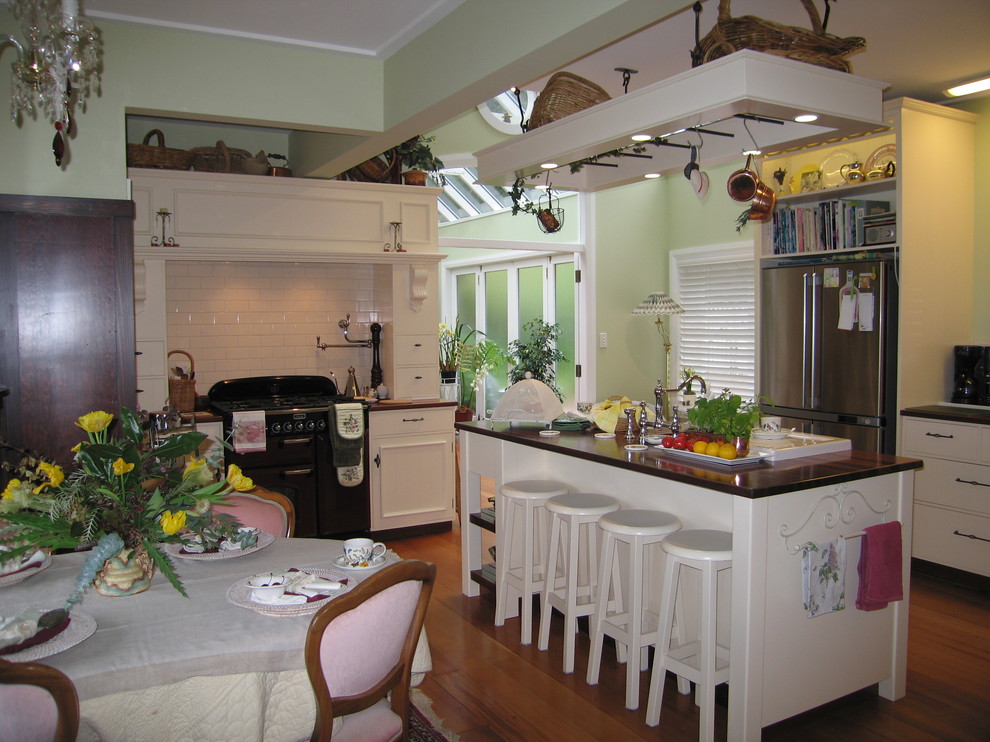 Photo of a mid-sized country u-shaped eat-in kitchen in Wellington with raised-panel cabinets, white cabinets, wood benchtops, white splashback, subway tile splashback, stainless steel appliances, medium hardwood floors, with island, green floor and brown benchtop.