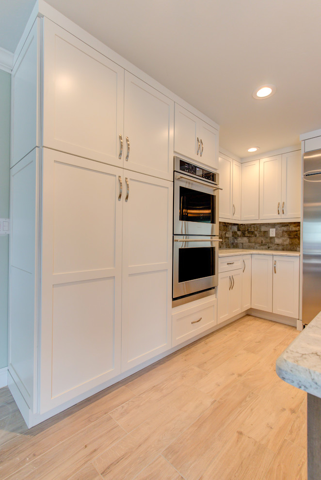 Enclosed kitchen - large transitional u-shaped porcelain tile and brown floor enclosed kitchen idea with an undermount sink, shaker cabinets, white cabinets, quartz countertops, brown backsplash, stainless steel appliances, an island and beige countertops