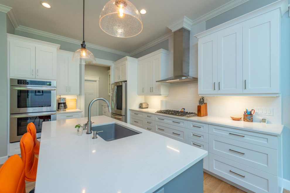 Inspiration for a mid-sized transitional l-shaped light wood floor and brown floor kitchen remodel with an undermount sink, shaker cabinets, white cabinets, quartzite countertops, white backsplash, ceramic backsplash, stainless steel appliances, an island and white countertops
