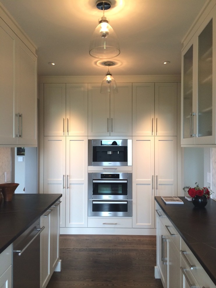 Photo of an expansive contemporary galley kitchen pantry in Boston with an undermount sink, recessed-panel cabinets, white cabinets, soapstone benchtops, white splashback, stone tile splashback, stainless steel appliances, dark hardwood floors and no island.