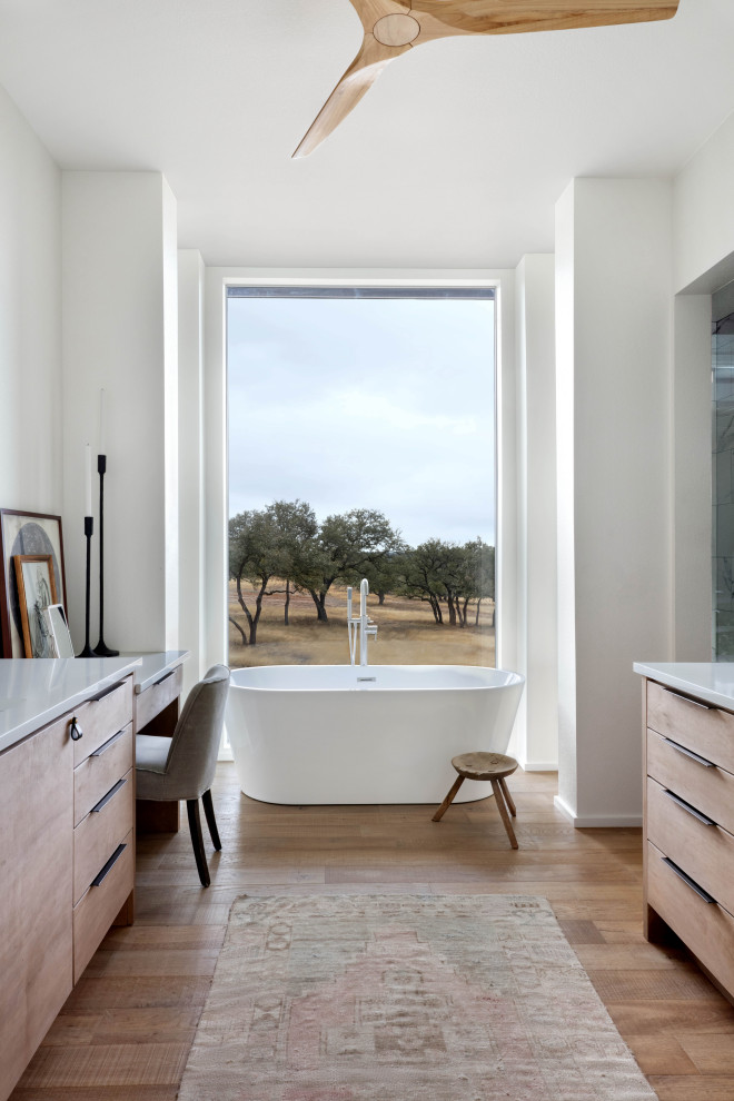 Landhausstil Badezimmer En Suite mit flächenbündigen Schrankfronten, hellen Holzschränken, freistehender Badewanne, weißer Wandfarbe, hellem Holzboden und weißer Waschtischplatte in Austin