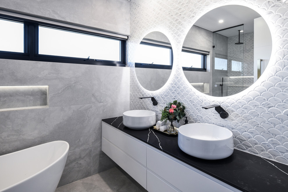 This is an example of a large contemporary ensuite bathroom in Sydney with all styles of cabinet, white cabinets, a freestanding bath, a double shower, a wall mounted toilet, multi-coloured tiles, mosaic tiles, a vessel sink, marble worktops, an open shower, black worktops, a wall niche, double sinks and a floating vanity unit.