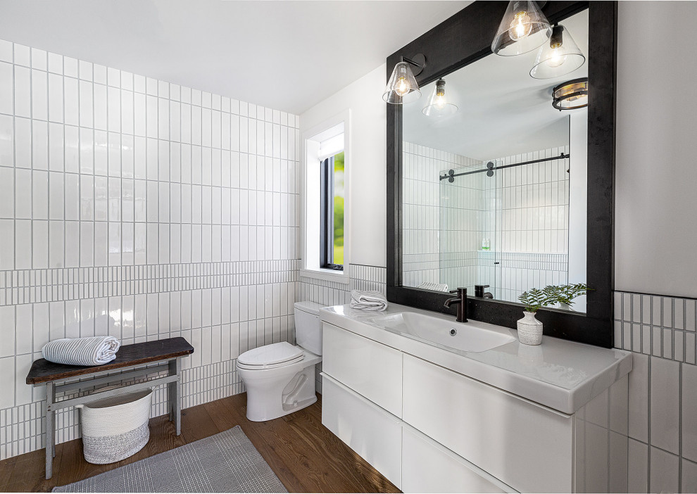 Mid-sized contemporary 3/4 bathroom in Burlington with flat-panel cabinets, white cabinets, an alcove shower, a one-piece toilet, white tile, ceramic tile, white walls, medium hardwood floors, an integrated sink, quartzite benchtops, a sliding shower screen, white benchtops, a single vanity and a floating vanity.