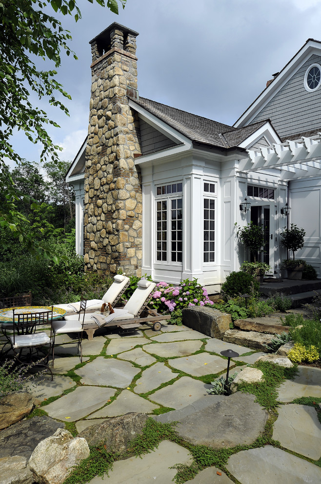 This is an example of a large traditional backyard patio in New York with natural stone pavers and a pergola.