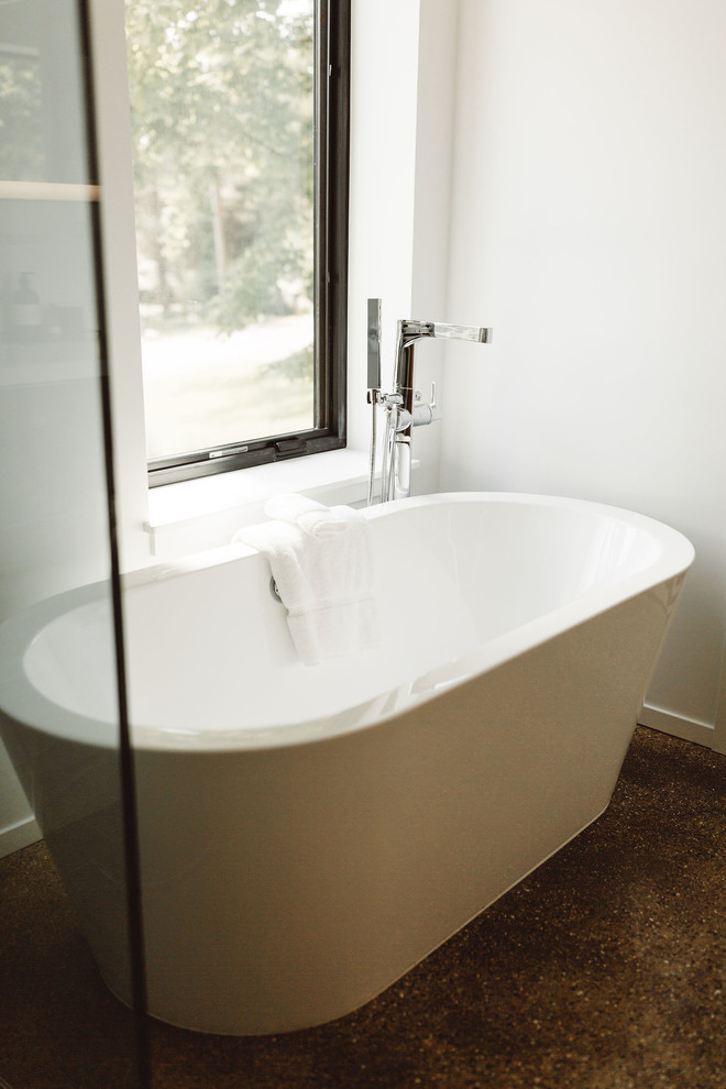 Photo of a modern bathroom in Grand Rapids with a freestanding tub, white walls, concrete floors and brown floor.