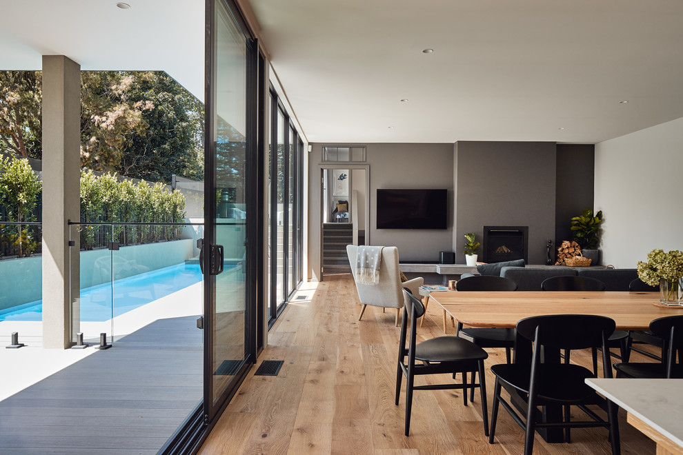 This is an example of a mid-sized contemporary open plan dining in Melbourne with grey walls, light hardwood floors, a standard fireplace, a concrete fireplace surround and brown floor.
