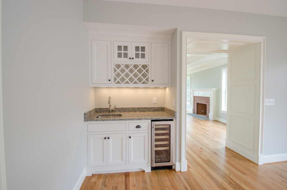 This is an example of a small traditional single-wall wet bar in Bridgeport with an undermount sink, beaded inset cabinets, white cabinets, granite benchtops, light hardwood floors and grey benchtop.