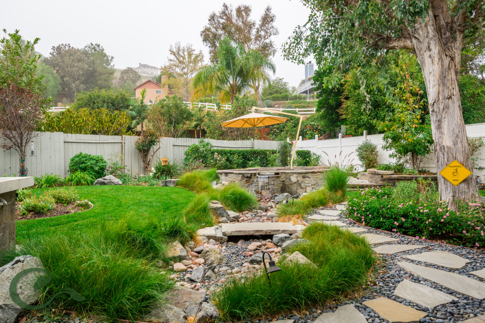 Photo of a mid-sized beach style backyard full sun xeriscape for spring in Orange County with a water feature, concrete pavers and a wood fence.