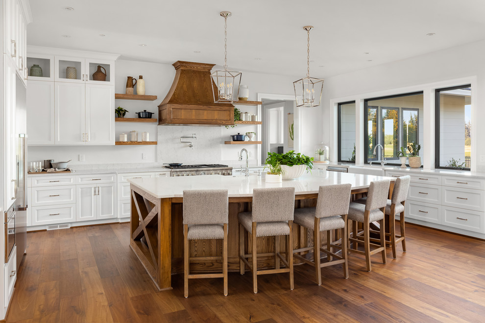 Inspiration for an expansive country u-shaped kitchen in Portland with a farmhouse sink, shaker cabinets, white cabinets, white splashback, stone slab splashback, stainless steel appliances, with island, brown floor, white benchtop, quartz benchtops and medium hardwood floors.
