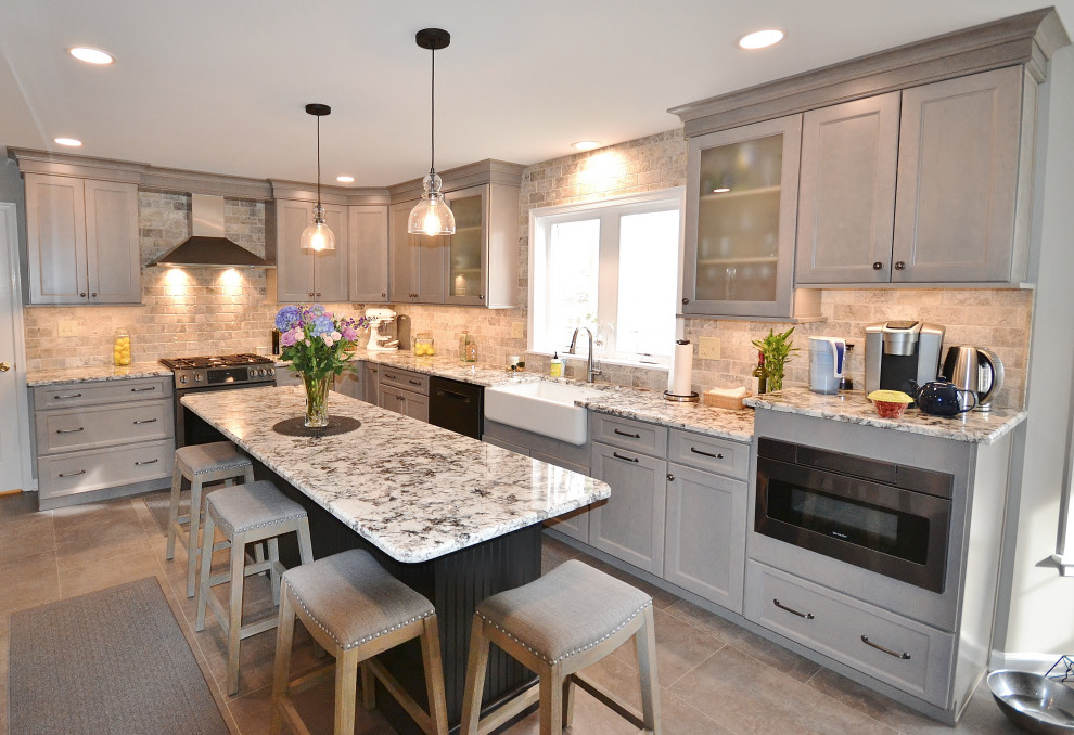 Large transitional l-shaped eat-in kitchen in Philadelphia with a farmhouse sink, raised-panel cabinets, grey cabinets, granite benchtops, beige splashback, travertine splashback, stainless steel appliances, vinyl floors, with island, beige floor and multi-coloured benchtop.