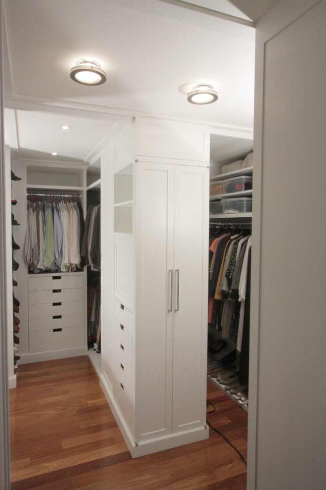 This is an example of a mid-sized transitional gender-neutral walk-in wardrobe in New York with flat-panel cabinets, white cabinets and medium hardwood floors.