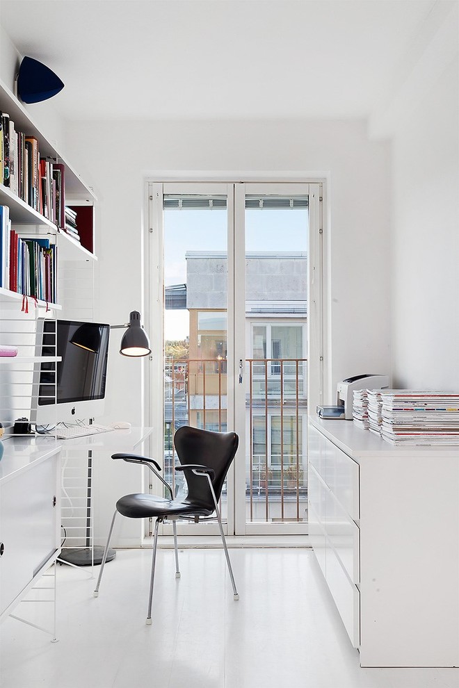 Photo of a small scandinavian study room in Stockholm with white walls, no fireplace, a built-in desk and painted wood floors.