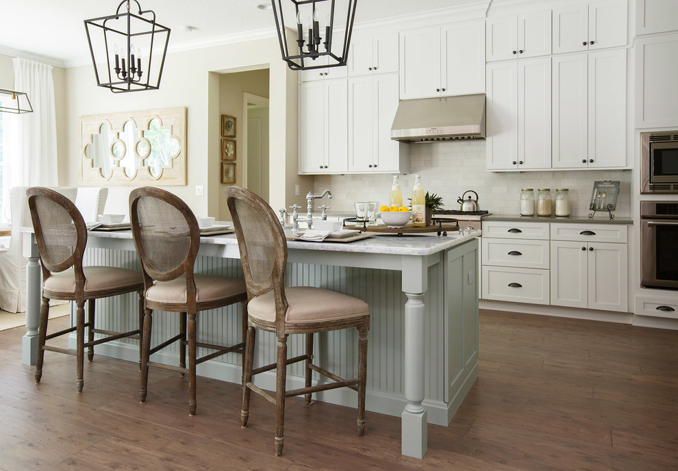 Design ideas for a large traditional galley kitchen in Jacksonville with shaker cabinets, white cabinets, white splashback, stainless steel appliances, dark hardwood floors, with island, an undermount sink, marble benchtops, porcelain splashback and brown floor.