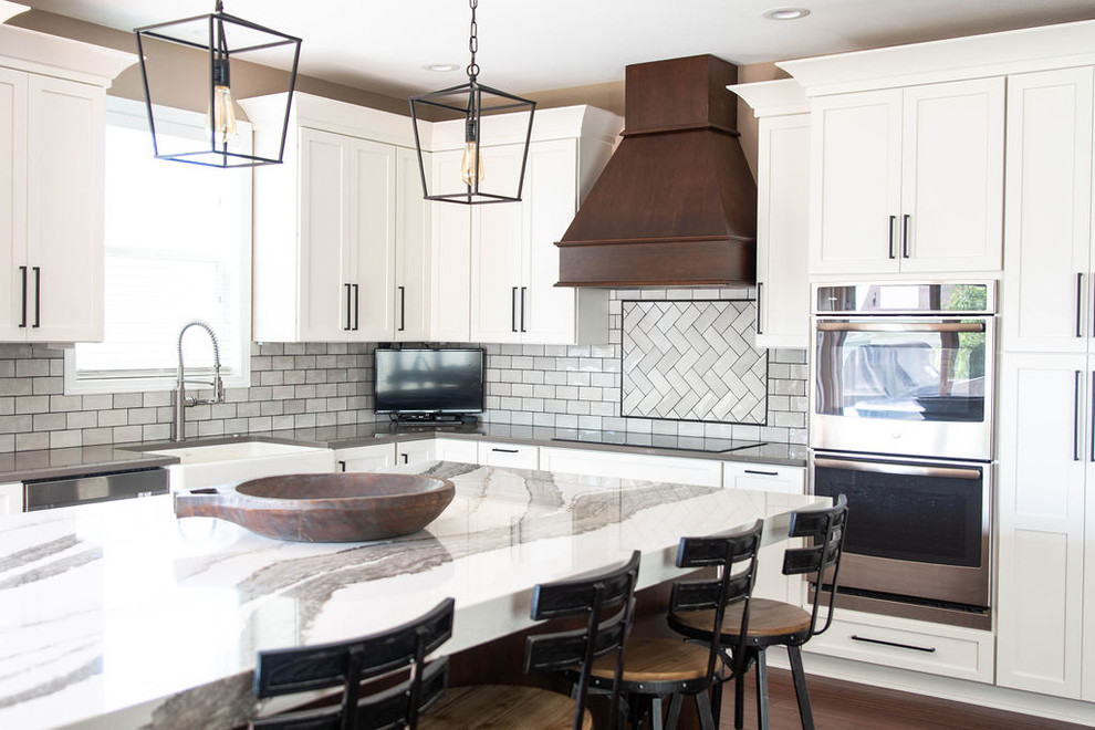 Example of a mid-sized transitional l-shaped medium tone wood floor and brown floor eat-in kitchen design in Omaha with a farmhouse sink, shaker cabinets, white cabinets, quartzite countertops, white backsplash, subway tile backsplash, stainless steel appliances, an island and white countertops