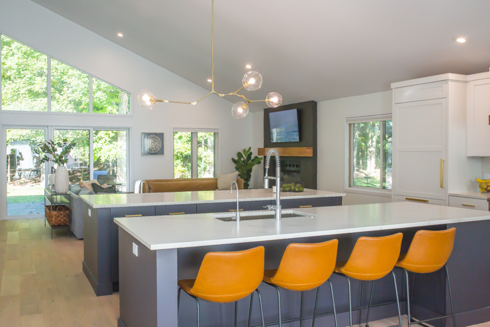 Large mid-century modern l-shaped light wood floor, beige floor and exposed beam eat-in kitchen photo in Detroit with a farmhouse sink, shaker cabinets, white cabinets, quartz countertops, white backsplash, quartz backsplash, stainless steel appliances, two islands and white countertops