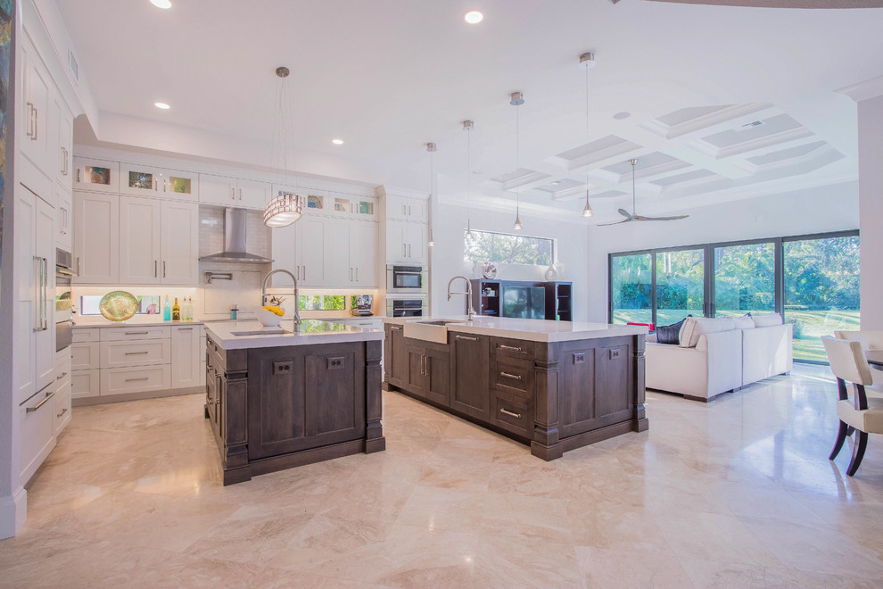Open concept kitchen - huge transitional l-shaped porcelain tile and beige floor open concept kitchen idea with a farmhouse sink, shaker cabinets, white cabinets, quartz countertops, white backsplash, porcelain backsplash, stainless steel appliances and two islands