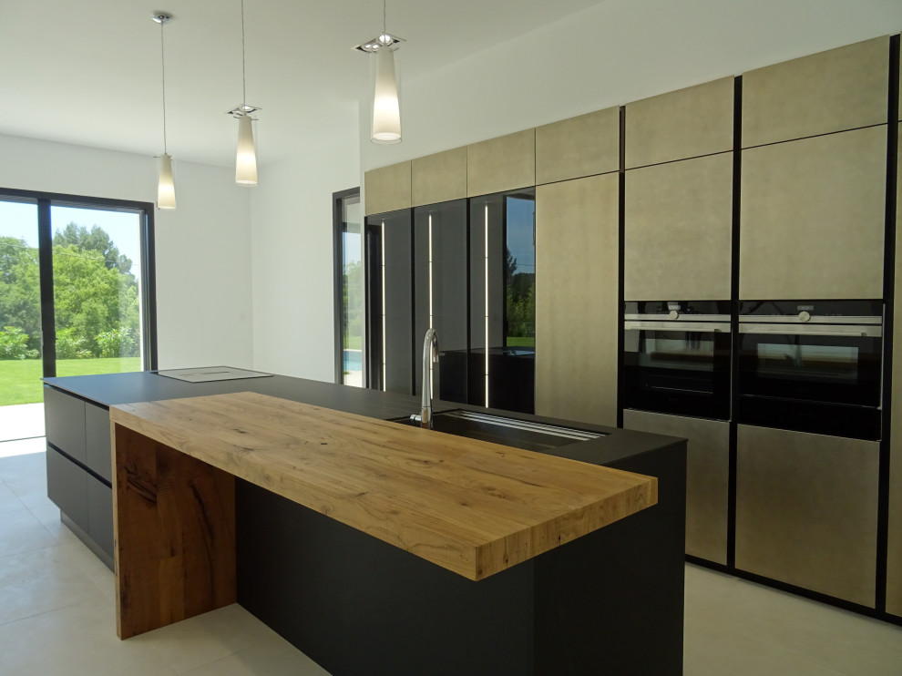 Design ideas for a large modern galley open plan kitchen in Marseille with an integrated sink, beaded inset cabinets, black cabinets, black appliances, ceramic floors, with island, beige floor and black benchtop.