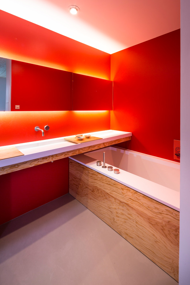 Large modern master bathroom in Munich with glass-front cabinets, a drop-in tub, red walls, a wall-mount sink and grey floor.